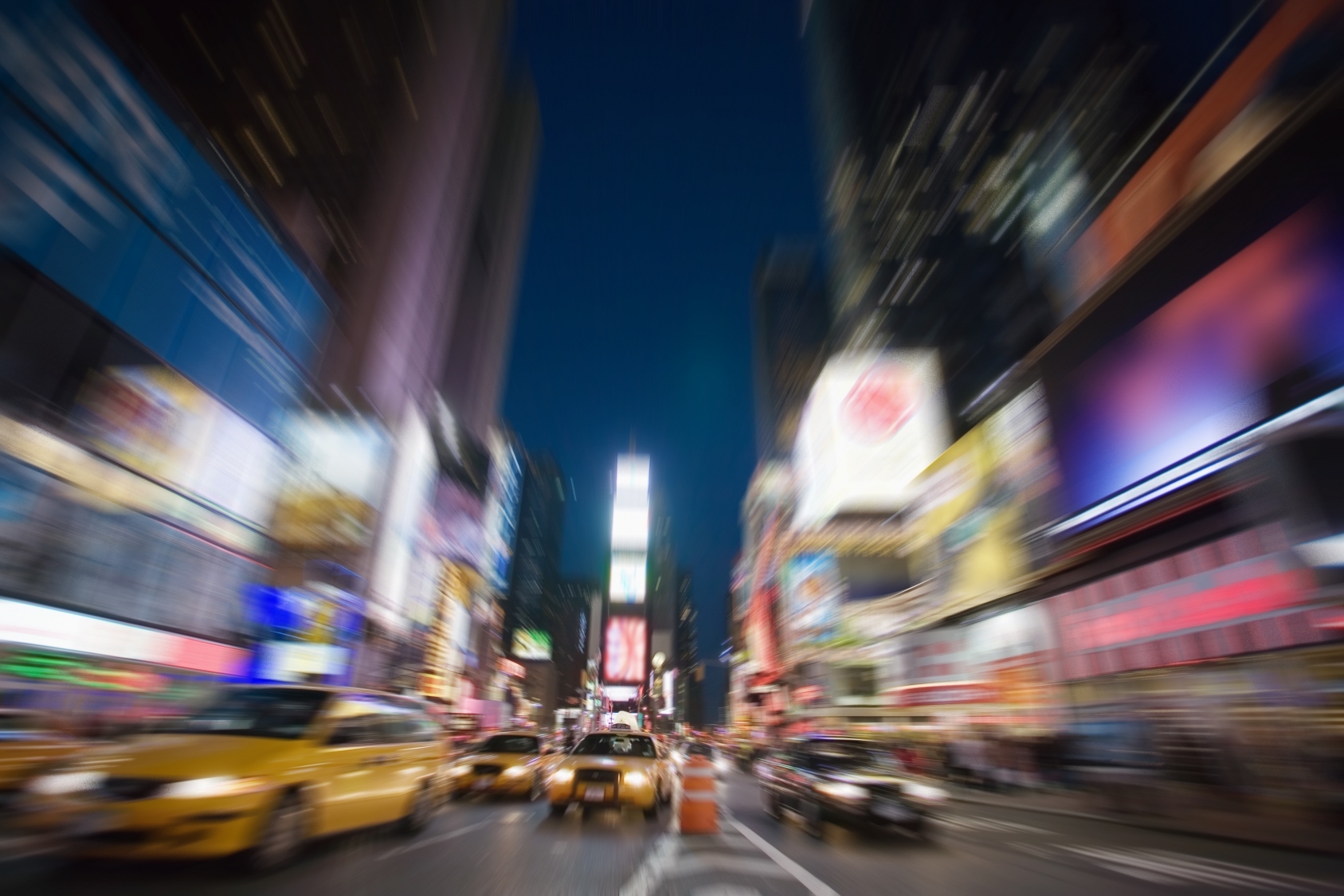 cars zoom past on broadway in times square at night.  radial blur